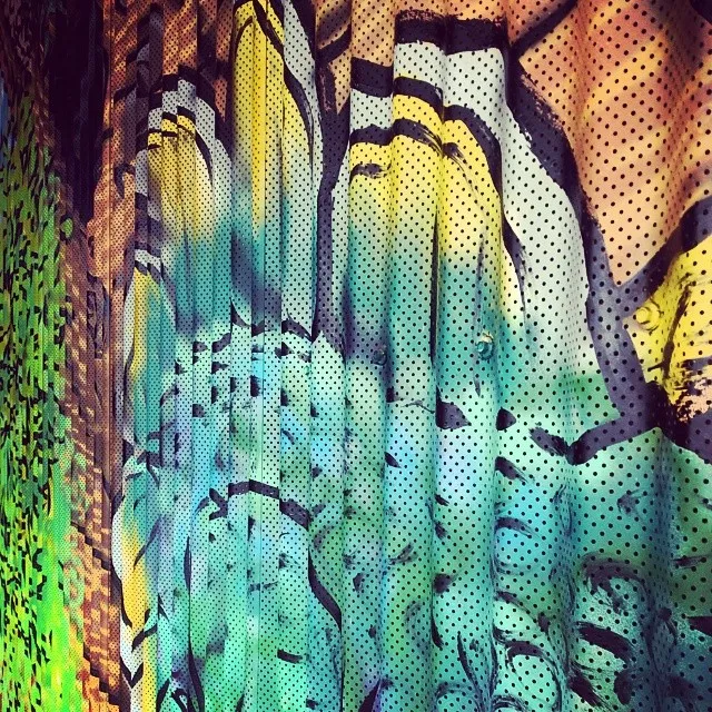 Close-up of a colorful mural with bold black linework painted on a corrugated, perforated metal surface