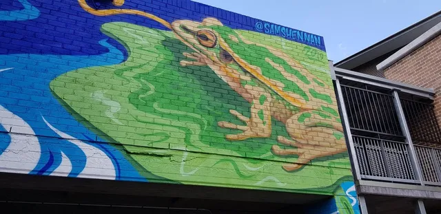 Brick wall mural of a large green and tan frog sitting on a lily pad over blue water
