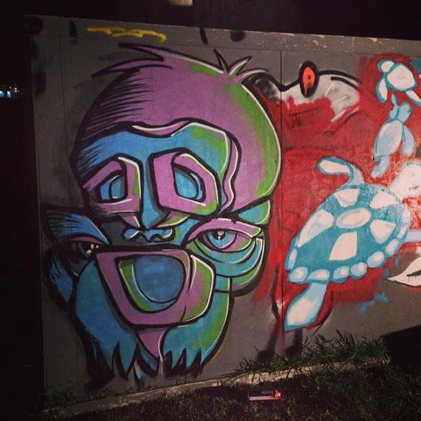 Graffiti mural of a psychedelic purple and green face next to a blue sea turtle on a red background