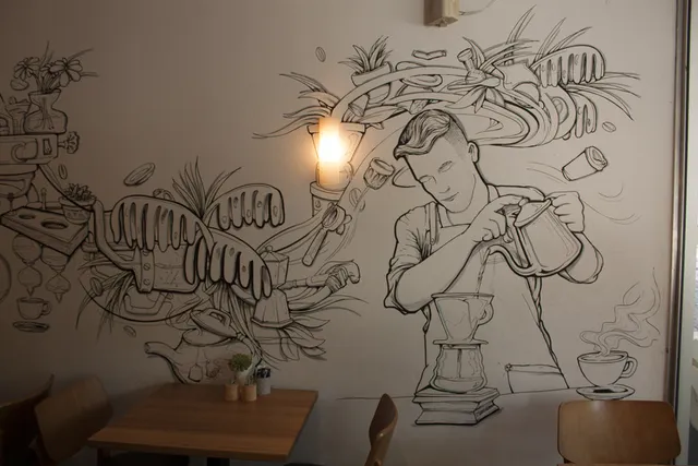 Black and white line art mural of a barista brewing pour-over coffee amidst swirling botanical and coffee elements