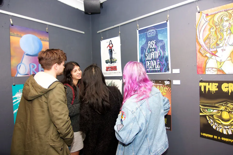 People at an exhibition viewing illustrated B-grade movie posters hanging on a dark wall