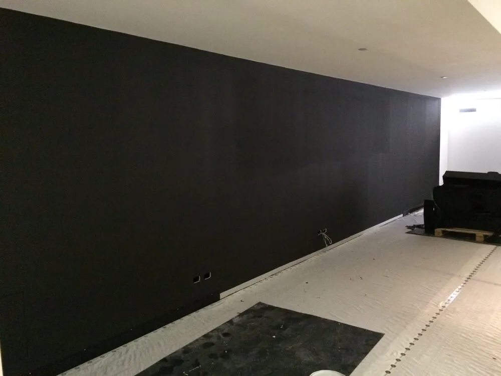 Blank black wall prepped for an indoor mural with protective sheeting on the floor
