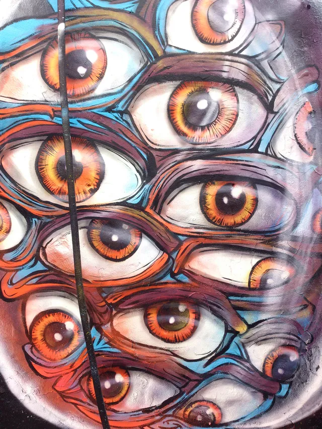 Mural detail of a dense cluster of staring eyes with orange irises and bold black outlines