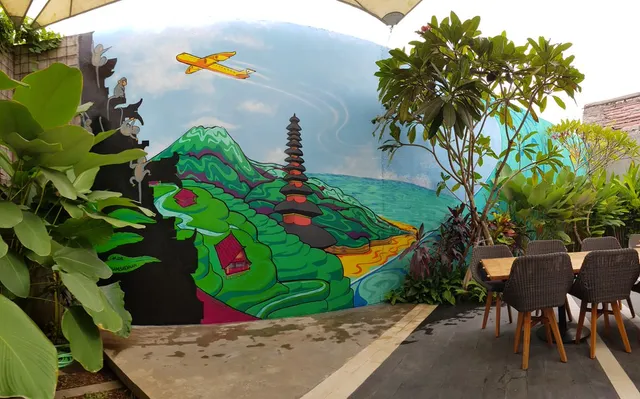 Outdoor mural of a vibrant landscape featuring green mountains, a tiered temple, cliffside monkeys and a yellow airplane