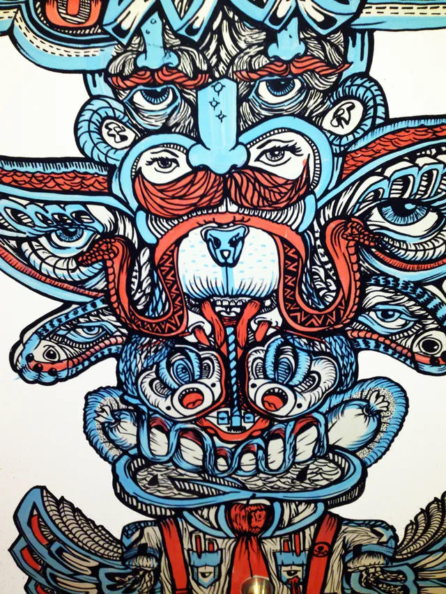 Mural of a symmetrical totemic face with multiple eyes and red mustaches in bold blue and red line work