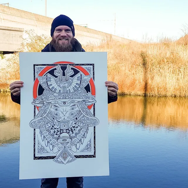 Man holding a large poster featuring a bold black line drawing of a symmetrical totemic animal mask with a red halo