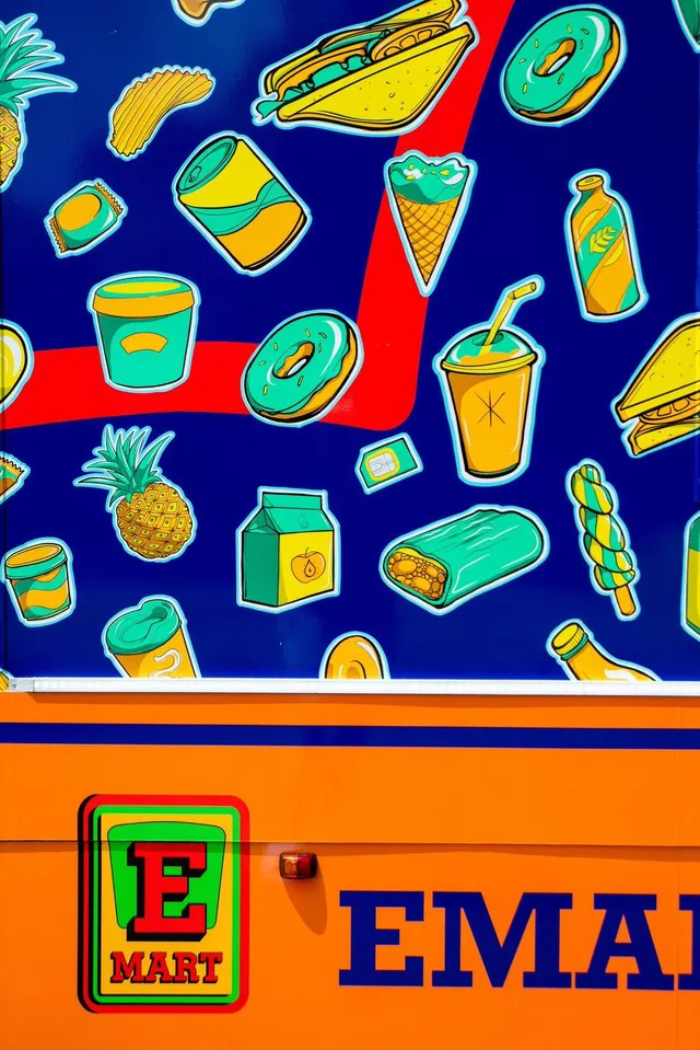 Vehicle wrap with bold, colorful illustrations of floating snacks and drinks above an orange E-Mart logo panel
