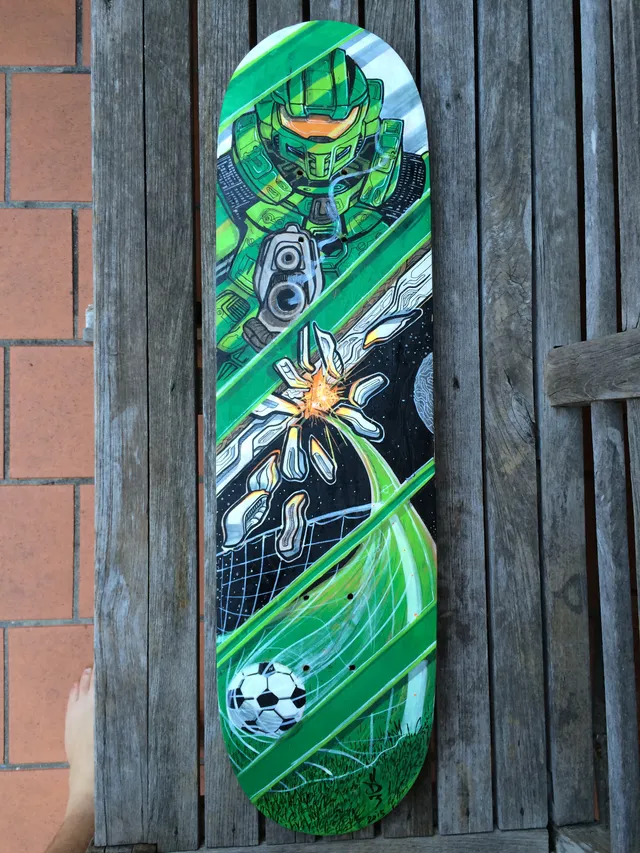 Painted skateboard showing a green armored sci-fi soldier, a space explosion, and a soccer ball hitting a net