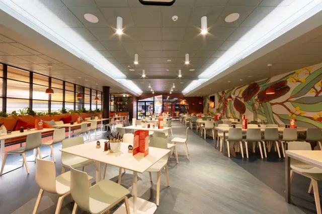 Wide shot of a restaurant interior featuring a large wall mural of oversized leaves and red flowers
