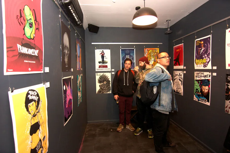 Three people viewing colorful illustrated posters hanging on dark walls at an art exhibition