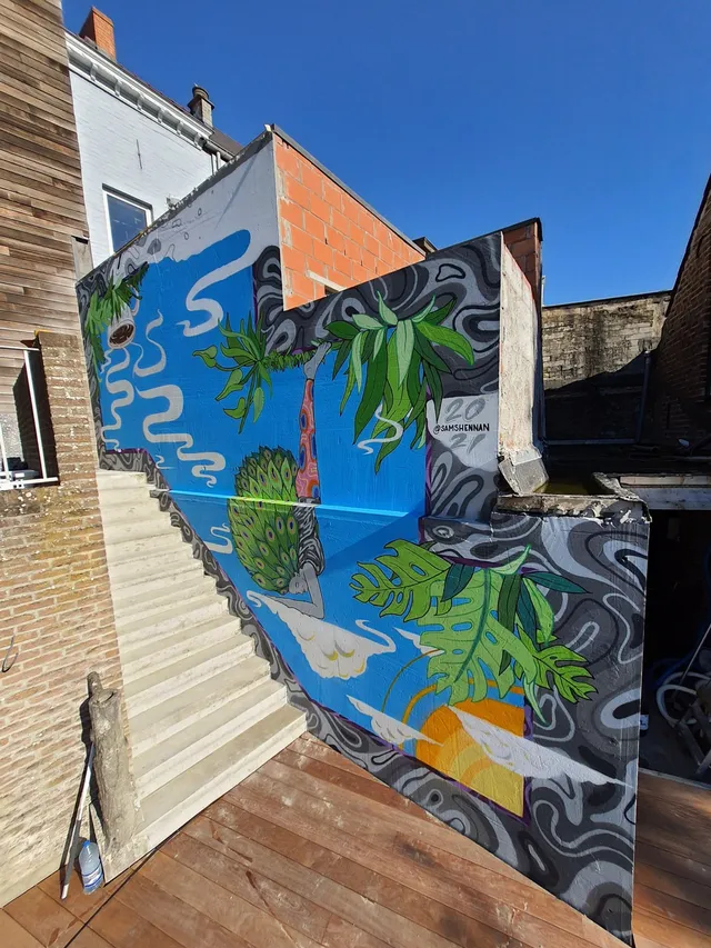 Mural on a staircase wall showing an upside-down figure with a leafy green headdress among tropical plants and clouds