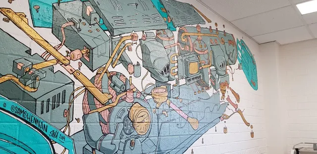 Exploded-view mural of espresso machine mechanics painted in teal, gold, and pink on a white brick wall