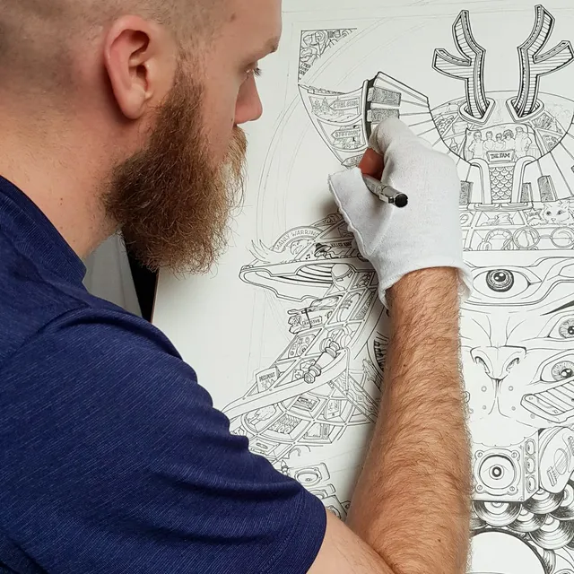 Bearded artist in a white glove inking a highly detailed, black and white totemic poster design