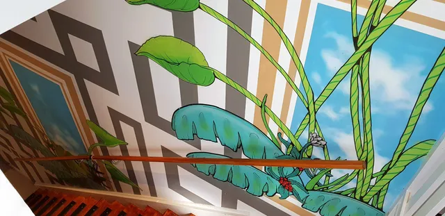 Stairwell mural with bold green leaves and vines overlapping geometric patterns and painted blue sky panels