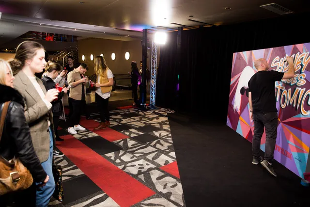 Artist live-painting a colorful Atomic Blonde mural at an indoor event while a crowd watches