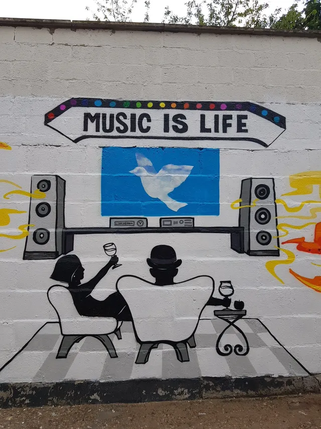 Mural of silhouetted figures drinking wine facing large speakers and a dove screen below a MUSIC IS LIFE sign