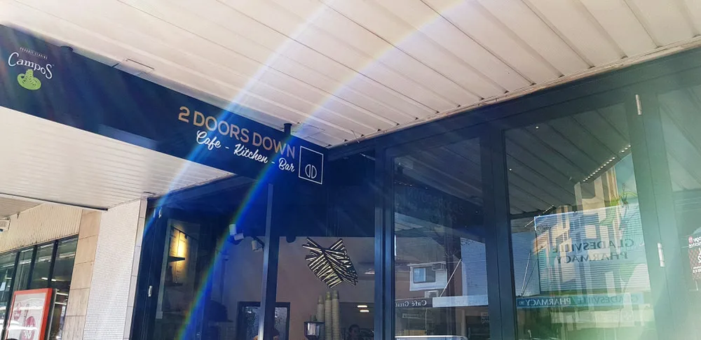 Exterior of 2 Doors Down Cafe with a blue sign above glass folding doors