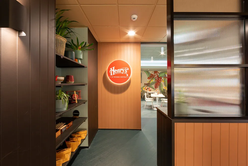 Restaurant entrance with a glowing Henry's sign and a view into a dining area featuring a botanical wall mural