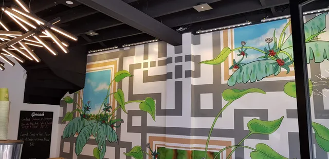 Cafe wall mural of geometric grey patterns intertwined with green leafy plants, red berries, and blue sky panels