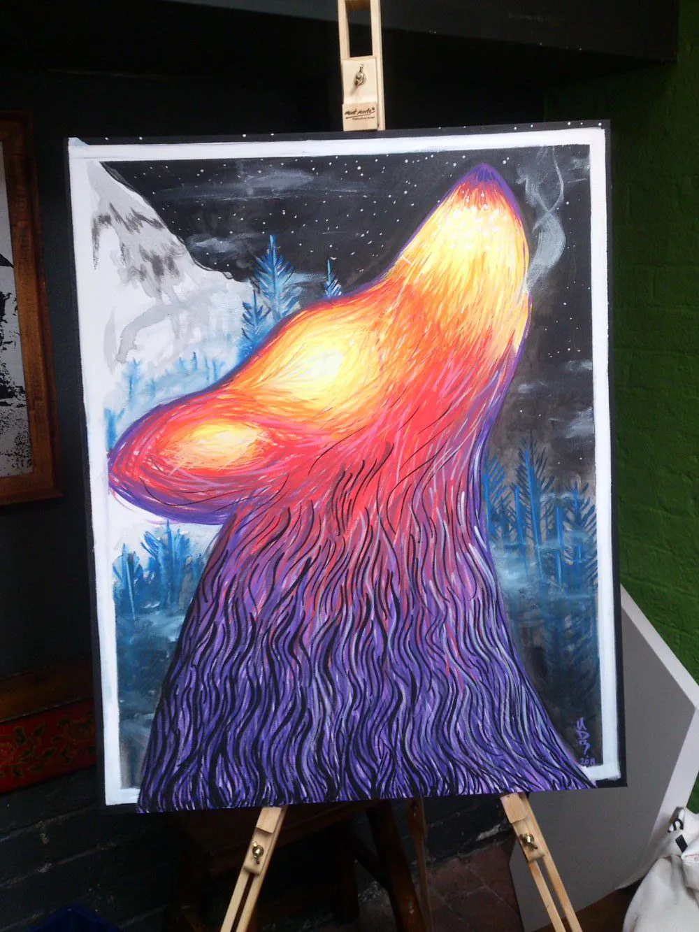 Painting on an easel of a psychedelic howling wolf with glowing fur against a starry mountain landscape