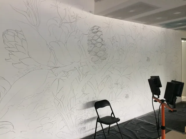 Sketched outline of a large floral mural on a white wall, with a folding chair and work lights in the foreground