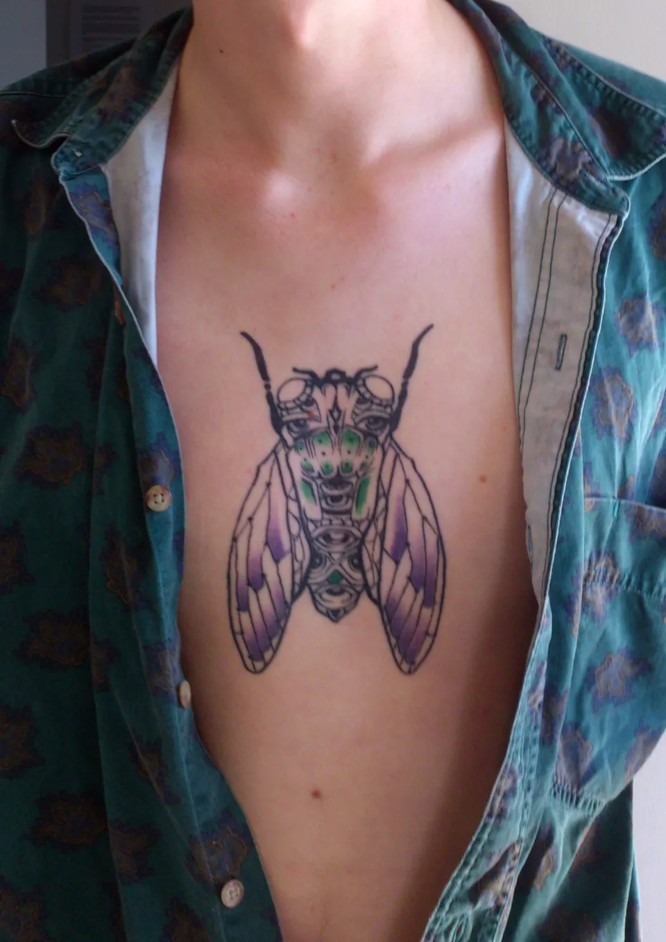 Bold line cicada tattoo with purple wings and green details on a person's chest