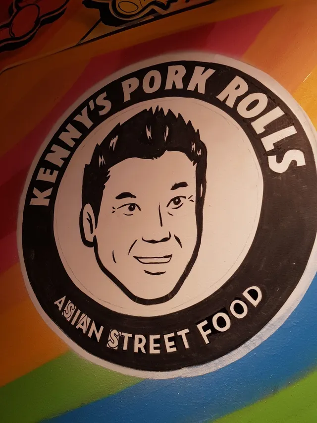 Painted mural of a circular Kenny's Pork Rolls logo with a black and white portrait on a colorful striped background