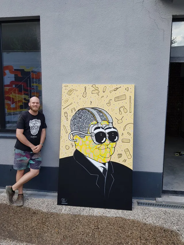 Man beside a large canvas painting of a psychedelic suited figure with goggles and a patterned face amid musical icons