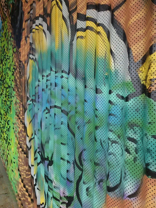 Close-up of a mural on a perforated corrugated metal shutter with bold black linework over vibrant colors