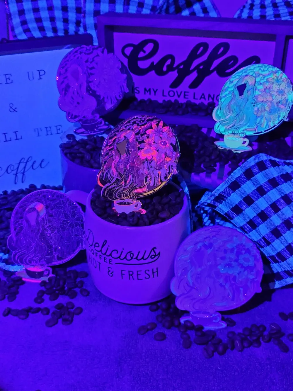 UV-reactive acrylic pins featuring psychedelic line art of a figure and flowers, displayed among coffee beans