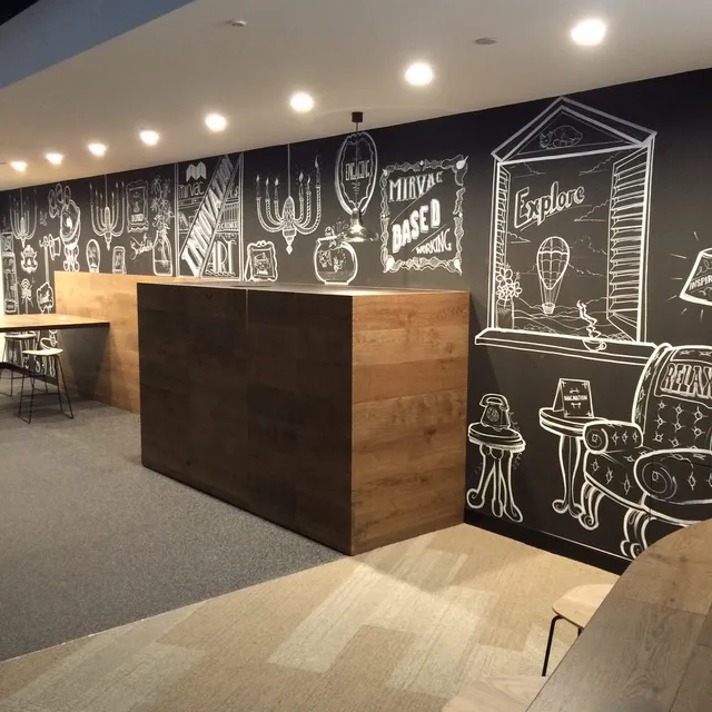 White line art mural on a black wall behind a wooden counter featuring illustrated furniture and typography