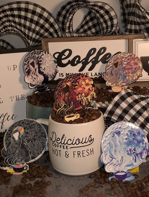 Five enamel pins of a psychedelic woman and floral patterns rising from a coffee cup, displayed among coffee beans