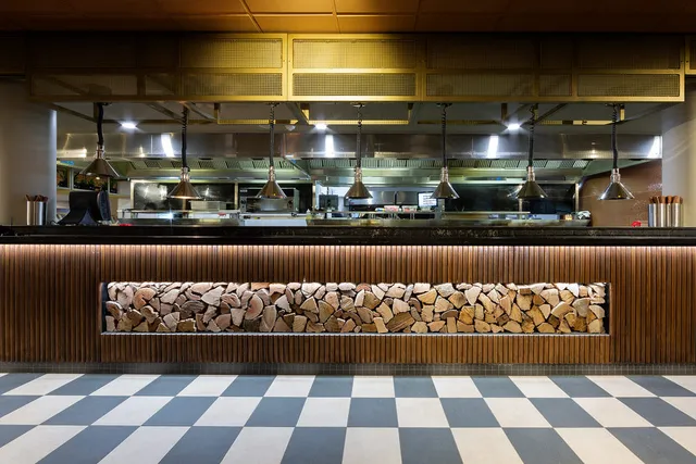 Restaurant counter with wood paneling, a recessed log stack, hanging heat lamps, and a view into an open kitchen