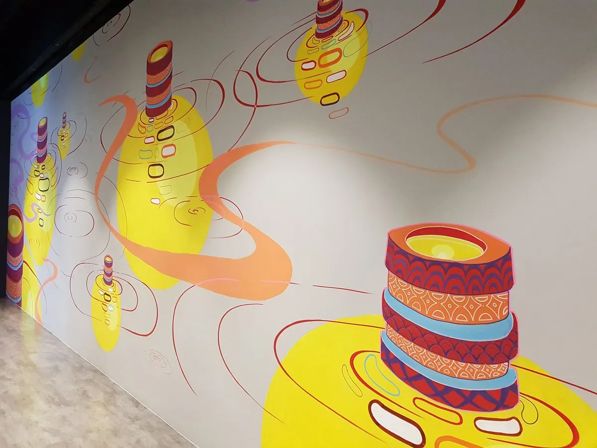 Indoor mural of abstract patterned cylinders in bright yellow pools with red ripple lines and flowing orange curves