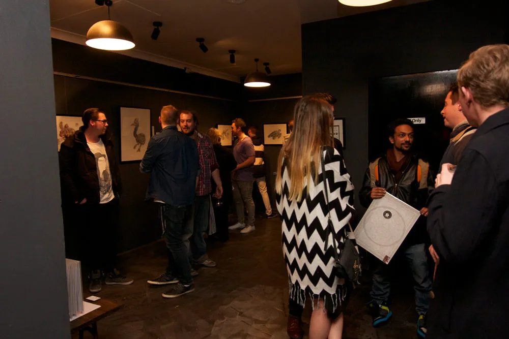 Opening night of a solo art exhibition with guests viewing framed drawings on dark gallery walls