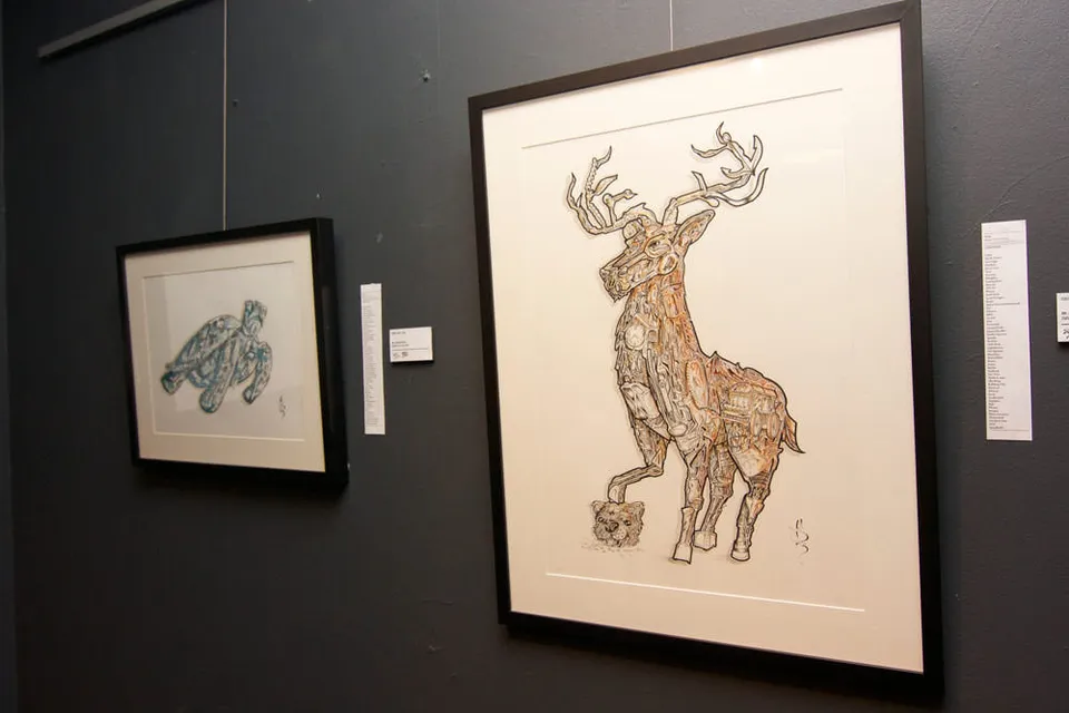 Two framed ink drawings on a dark gallery wall featuring a blue sea turtle and an intricately detailed stag