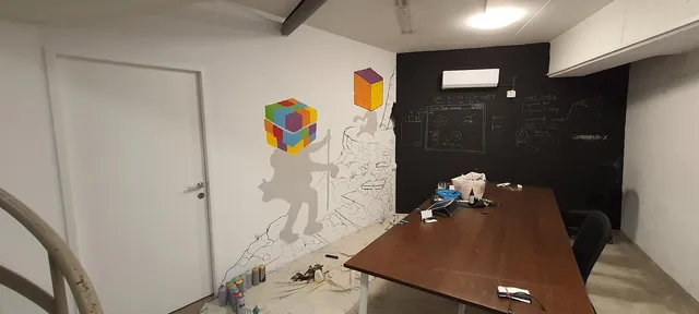 Unfinished office mural of grey figures with colorful 3D cube heads climbing a sketched rocky path