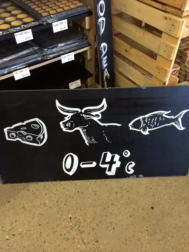 Hand-painted black sign with white line art of a cheese wedge, bull head, and fish above the text 0-4°c