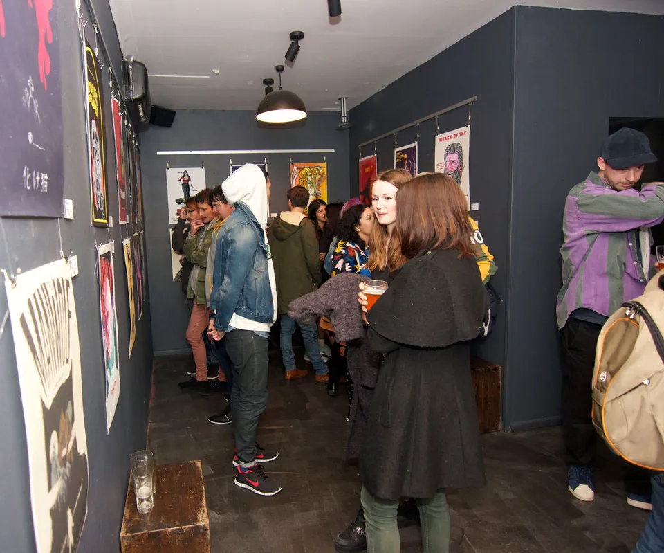 People socializing and viewing illustrated posters hung on dark walls at an art exhibition