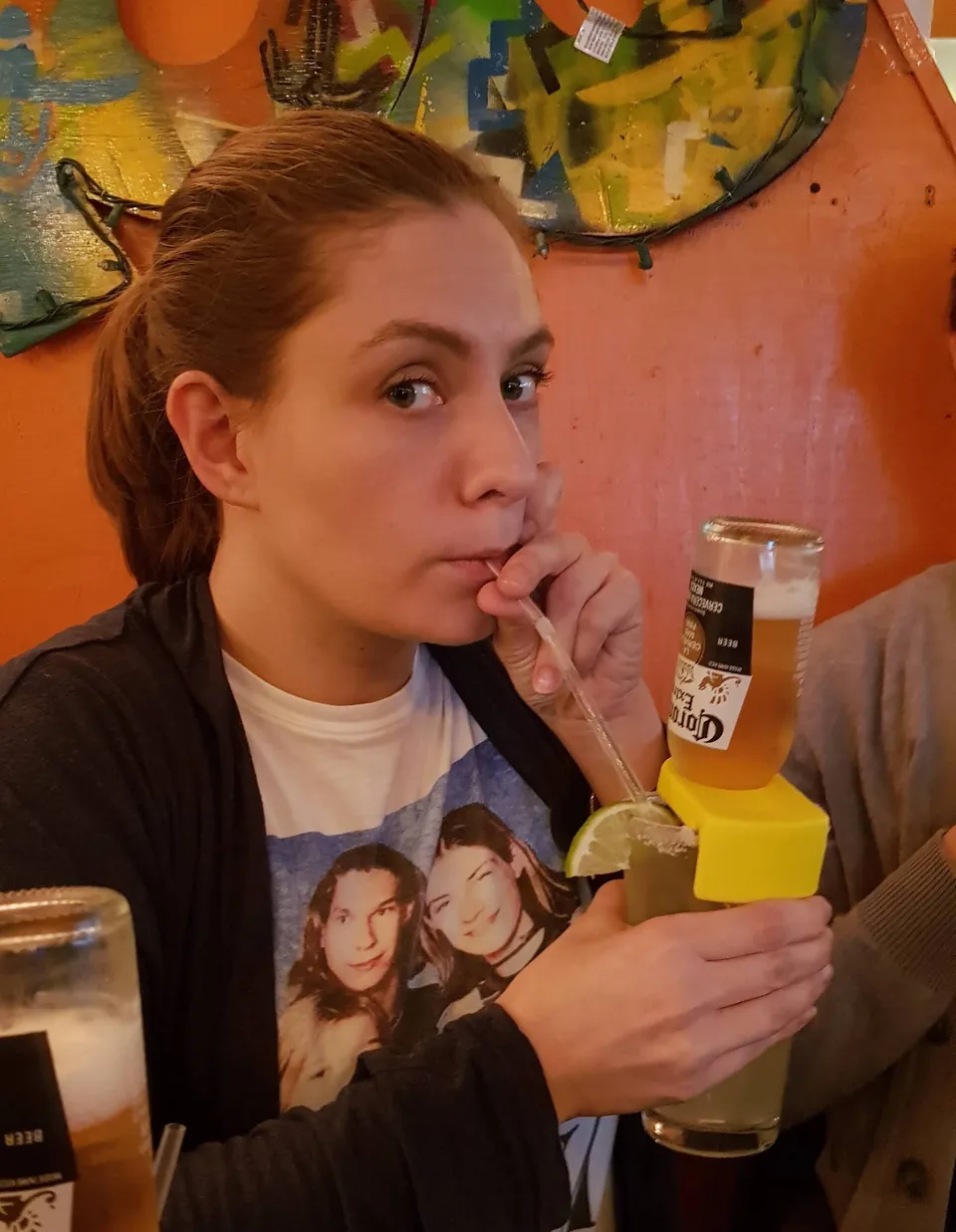 Person drinking a beer cocktail with a straw and lime, looking at the camera