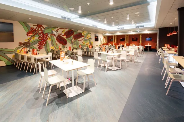 Wall mural of oversized red banksia flowers, green leaves, and a white cockatoo in a modern restaurant dining room