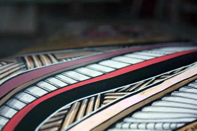 Detail of a painted skateboard showing bold sweeping linework and striped geometric patterns in red, black and white