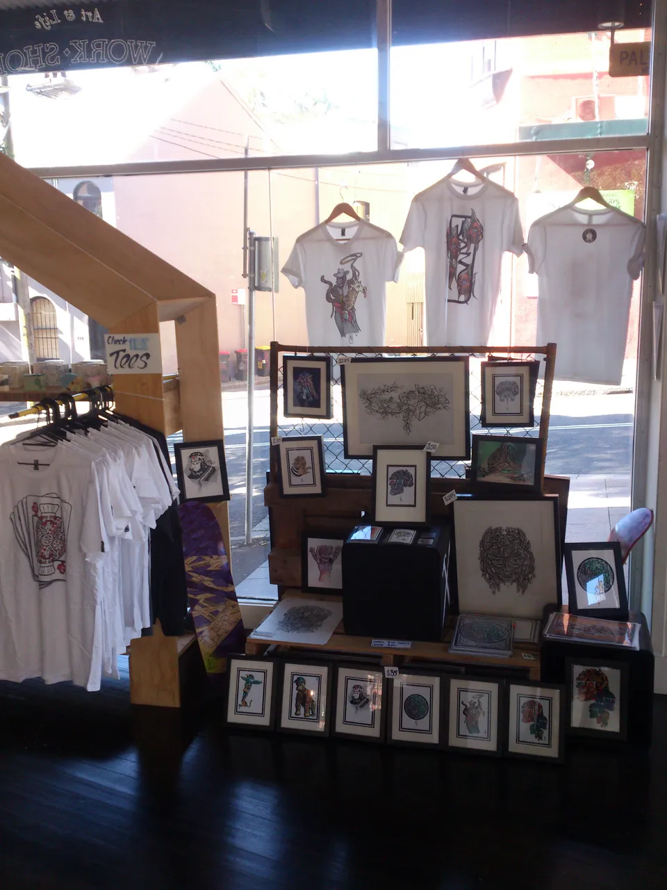 Shop window display of framed psychedelic prints, graphic t-shirts, and a painted skateboard