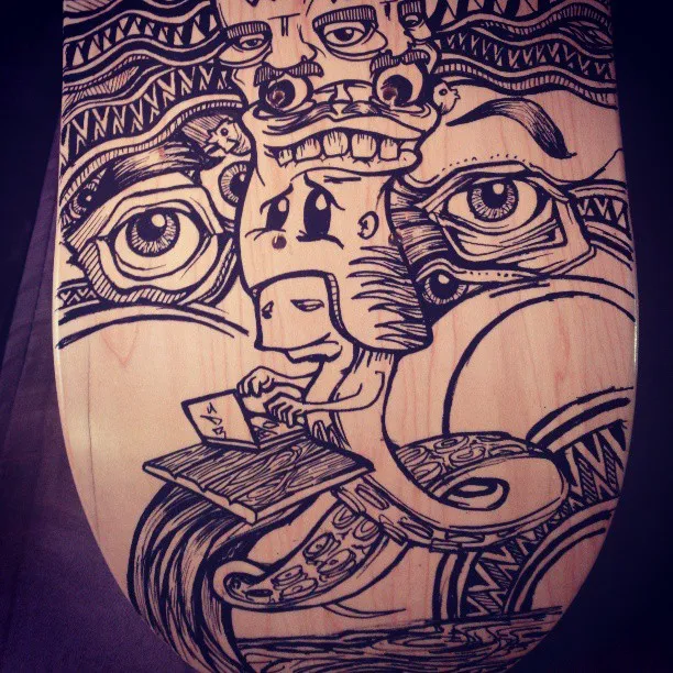 Ink drawing on a skateboard deck of a tentacled creature typing on a laptop beneath stacked totemic faces and giant eyes