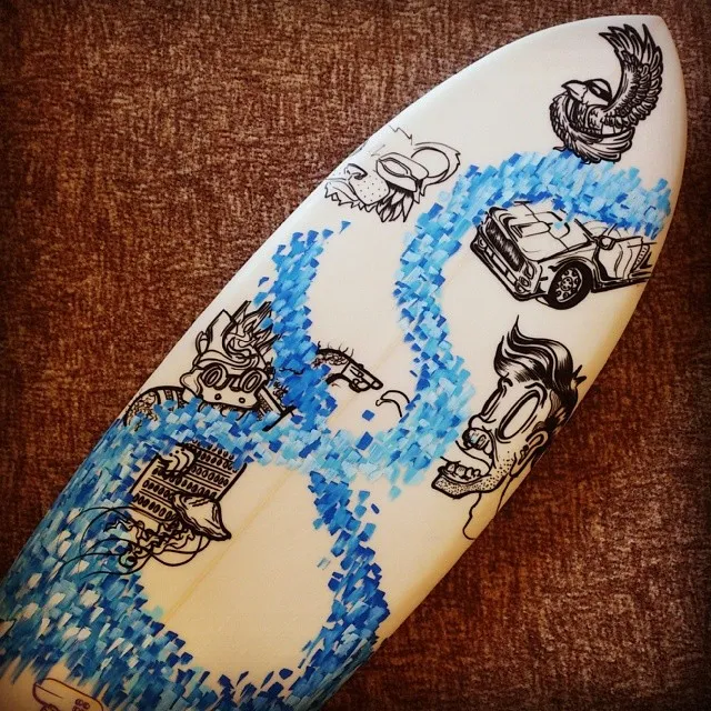Hand-painted surfboard with black line art of a face, car, and bird, intertwined with a pixelated blue wave
