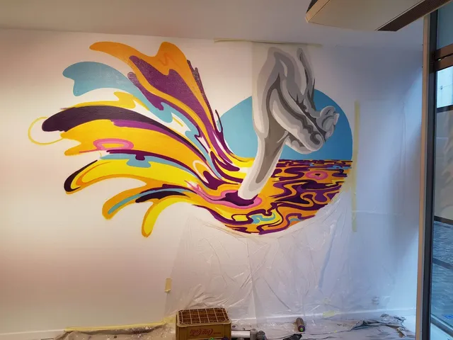 In-progress mural of a stylized grey hand emerging from a psychedelic splash of yellow, purple and blue