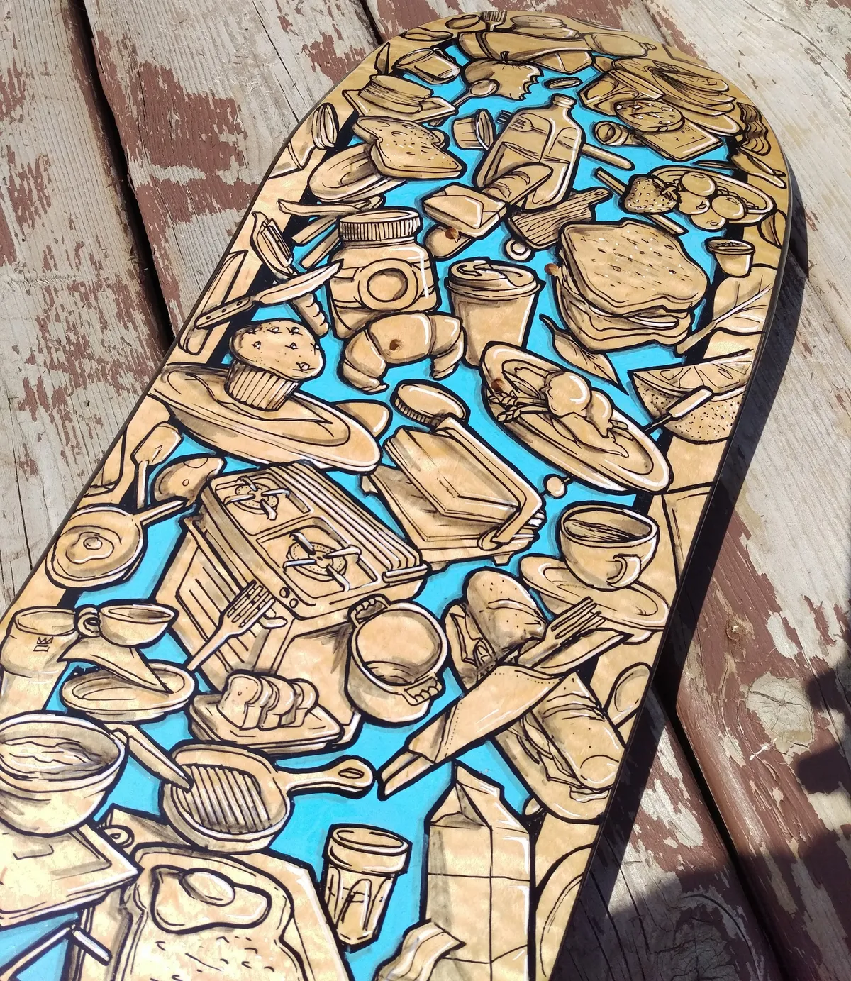 Painted skateboard deck featuring a dense collage of breakfast foods and kitchenware against a bright blue background