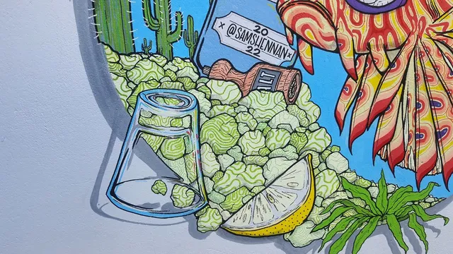 Mural detail of an overturned shot glass, lime wedge, salt shaker, and cacti next to brightly patterned lionfish fins