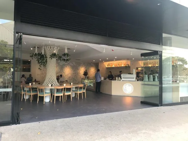 Open cafe interior with a subtle line art mural on the back wall behind a circular table and large macrame tree