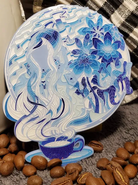 Blue and white enamel pin of a woman and flowers formed by steam rising from a coffee cup, resting among coffee beans